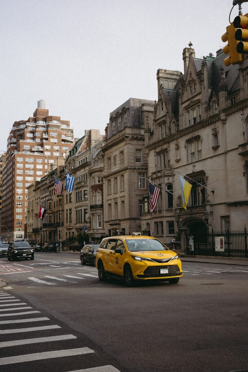 A yellow car driving down a street next to tall buildings