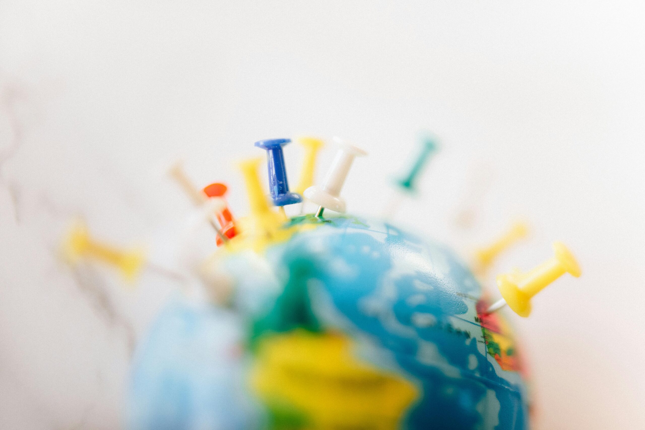 Vibrant close-up of a globe marked with multicolored push pins on a white background.