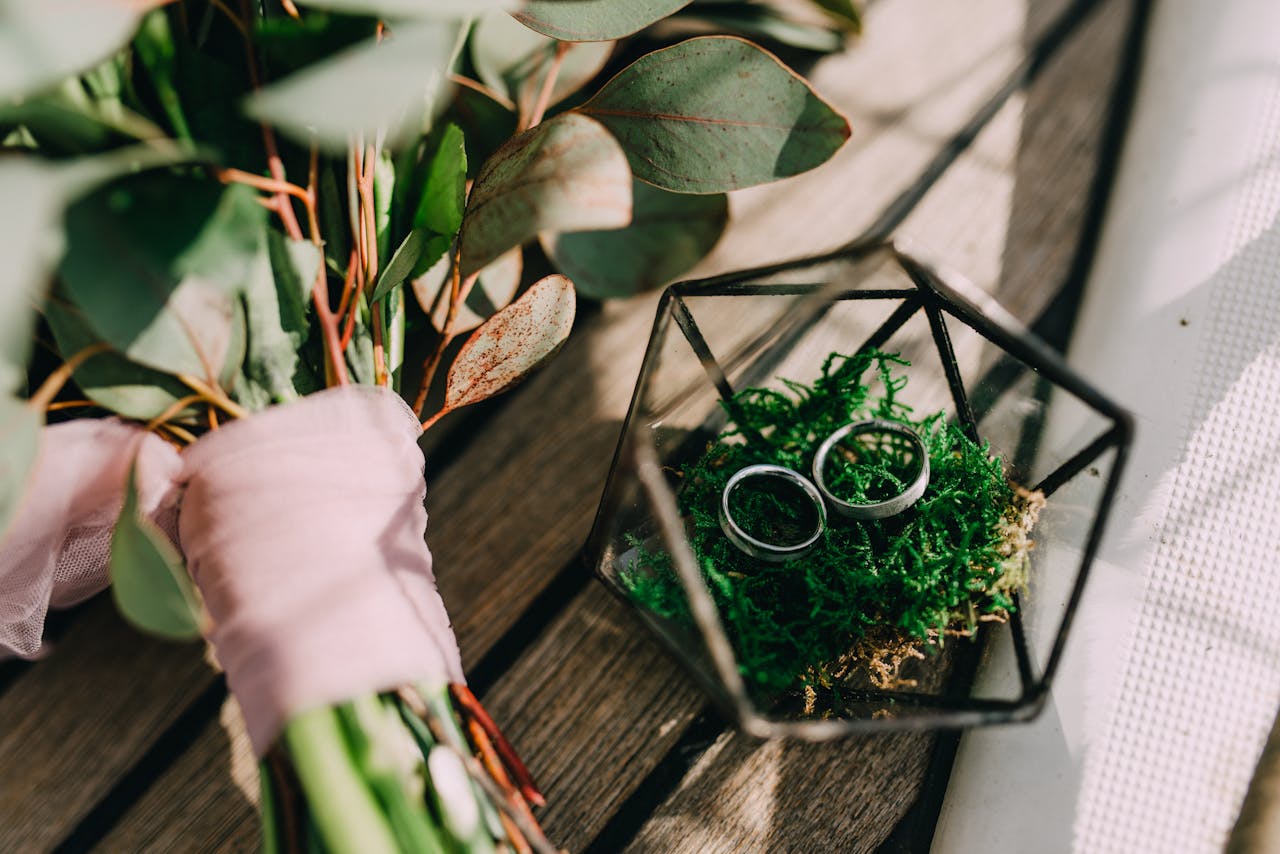 A wedding bouquet with eucalyptus and rings in a geometric holder on a wooden surface.