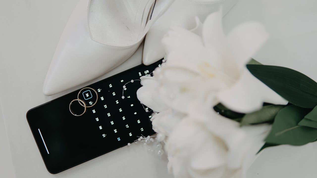Flat lay of wedding essentials including high heels, rings, and a bouquet on a calendar.